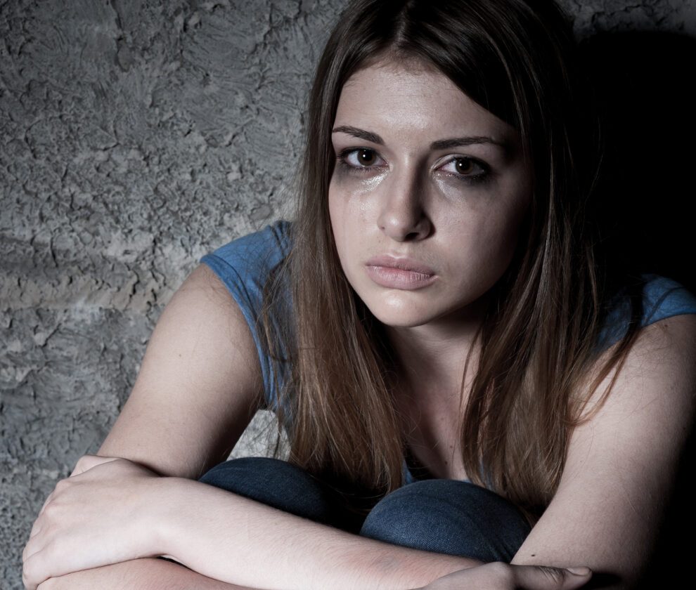 Hopelessness. Top view of young woman crying and looking at camera while sitting against dark wall