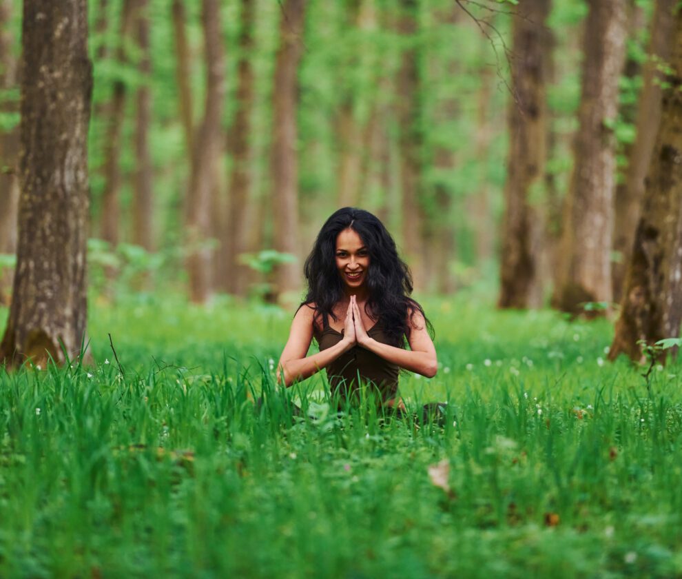 Positive brunette in casual clothes meditating in the forest at daytime