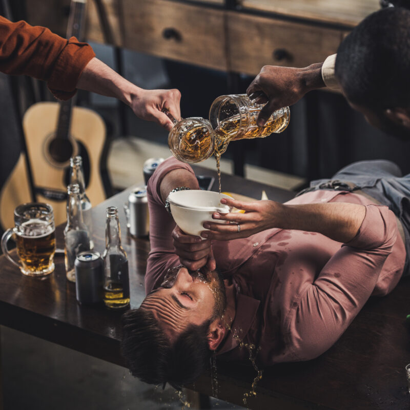 A group of friends pouring alcohol down on friends throat. They're trying to figure out what is the most addictive drug