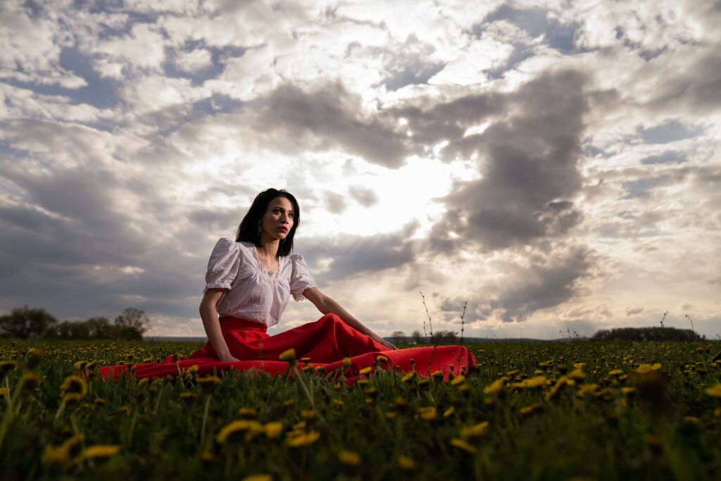 A young woman sitting in a field under the clouds looking for the best rehabs in Florida